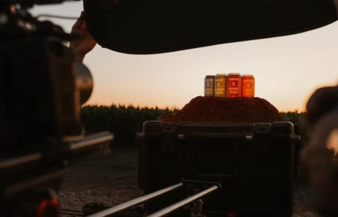 Cans of flavored drinks displayed on a mound of spice during a sunset product photoshoot in an outdoor setting.