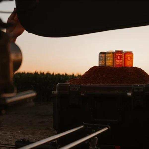 Cans of flavored drinks displayed on a mound of spice during a sunset product photoshoot in an outdoor setting.