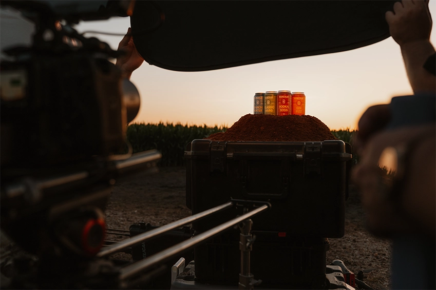 Cans of flavored drinks displayed on a mound of spice during a sunset product photoshoot in an outdoor setting.