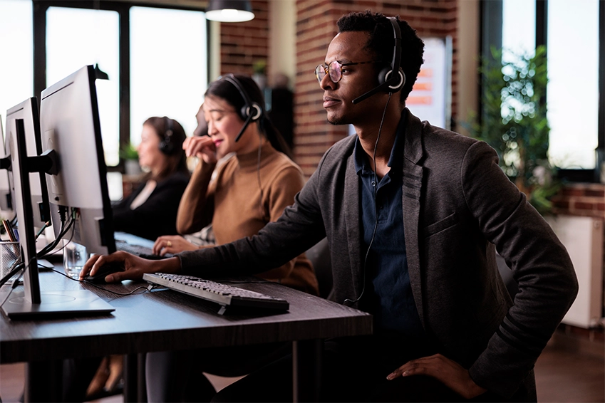 Customer support specialists working at computers with headsets in a modern office call center.