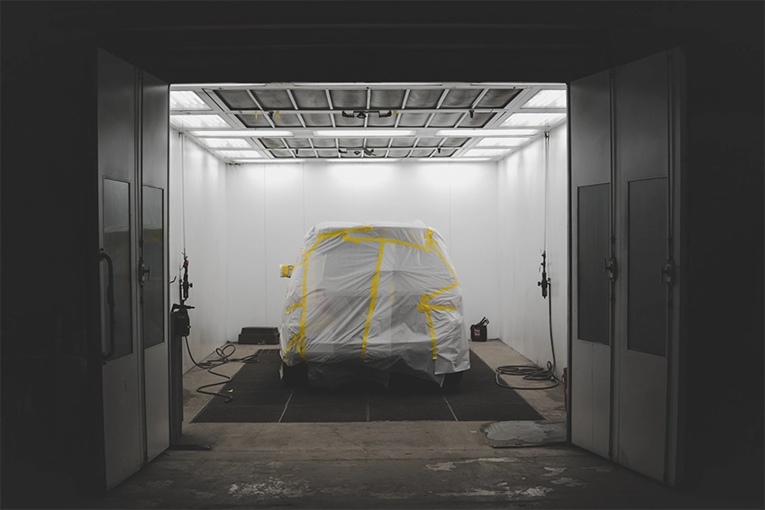 Vehicle covered with masking film and tape inside an auto body paint booth prepared for refinishing.