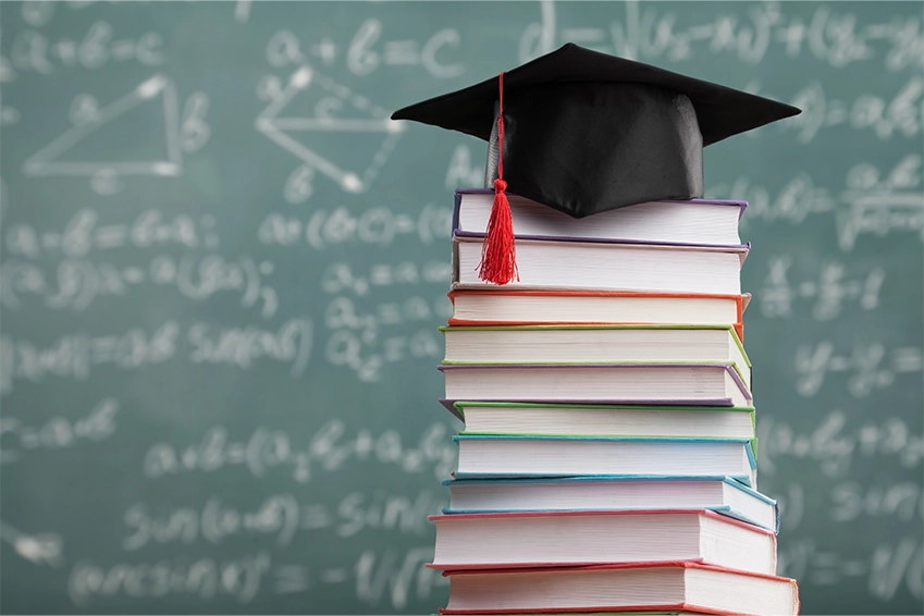 Graduation cap on top of stacked books in front of a chalkboard — educational branding and academic marketing visuals.