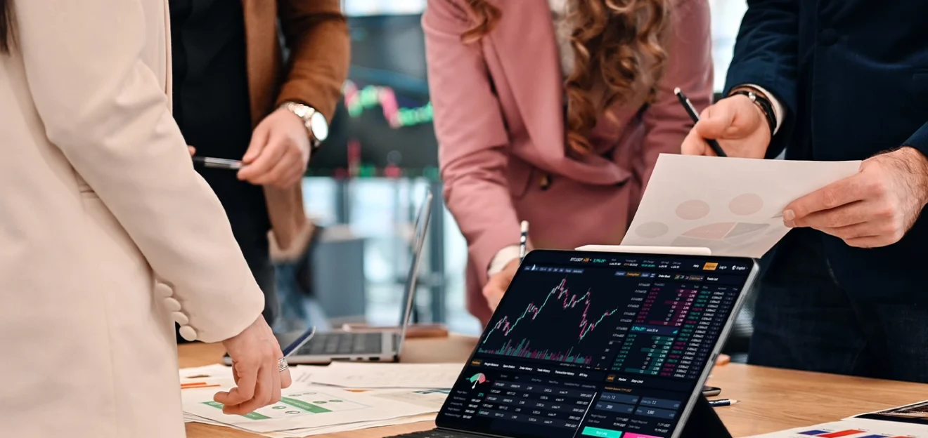Business professionals analyzing financial data and stock market charts on a tablet during a strategy meeting.