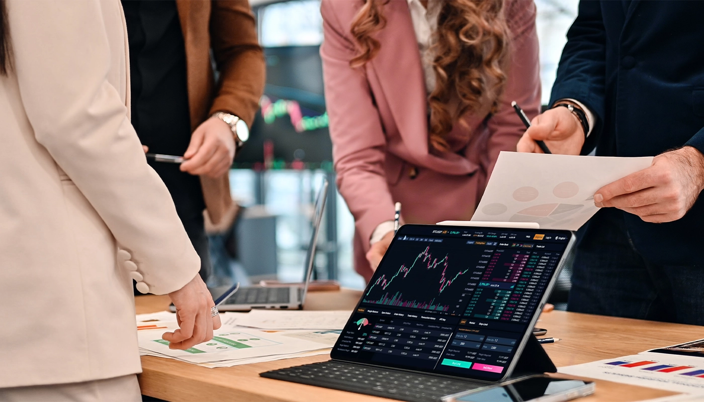 Business professionals analyzing financial data and stock market charts on a tablet during a strategy meeting.