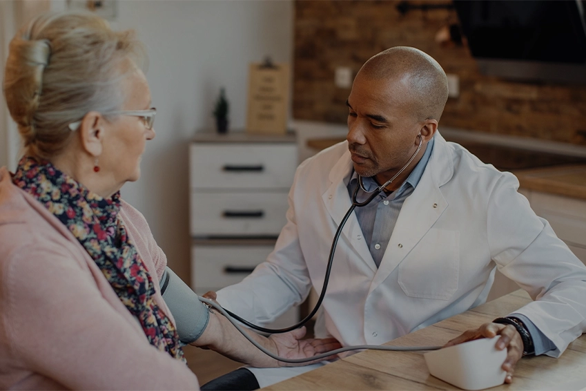 Doctor checking a senior woman’s blood pressure during a home medical consultation.