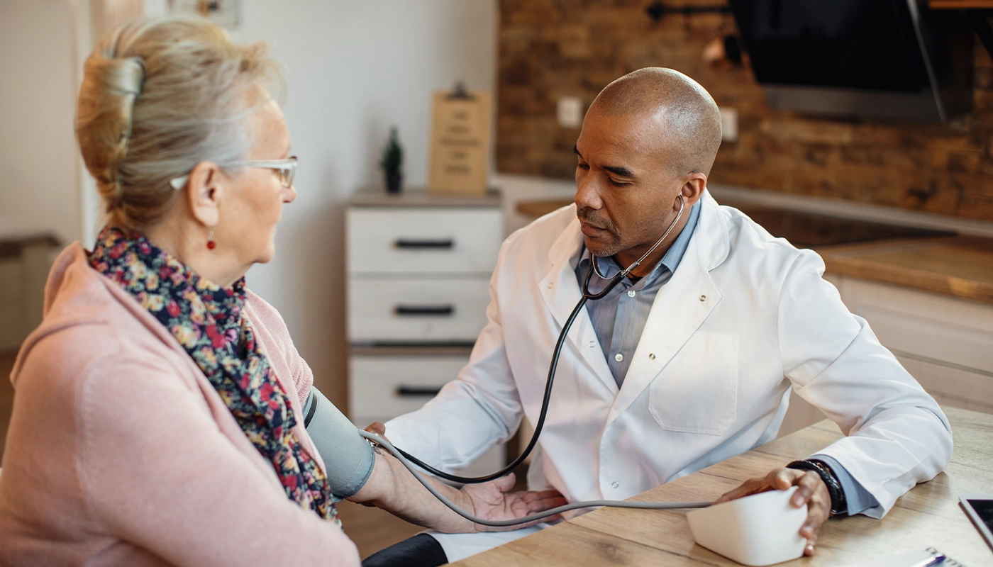 Doctor checking a senior woman’s blood pressure during a home medical consultation.