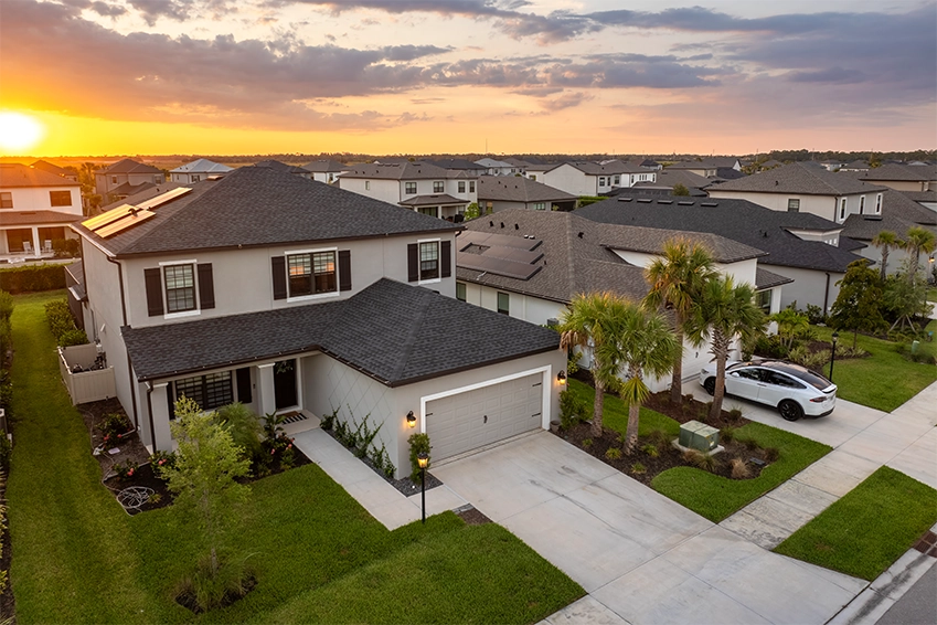 Modern suburban home with solar panels and a driveway at sunset in a residential neighborhood.