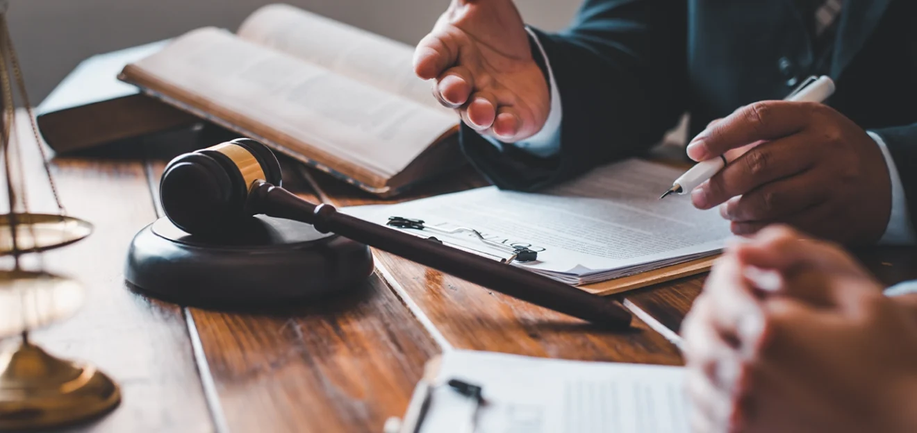 Close-up of a lawyer consulting a client with legal documents, gavel, and open law books on a wooden desk in an office.