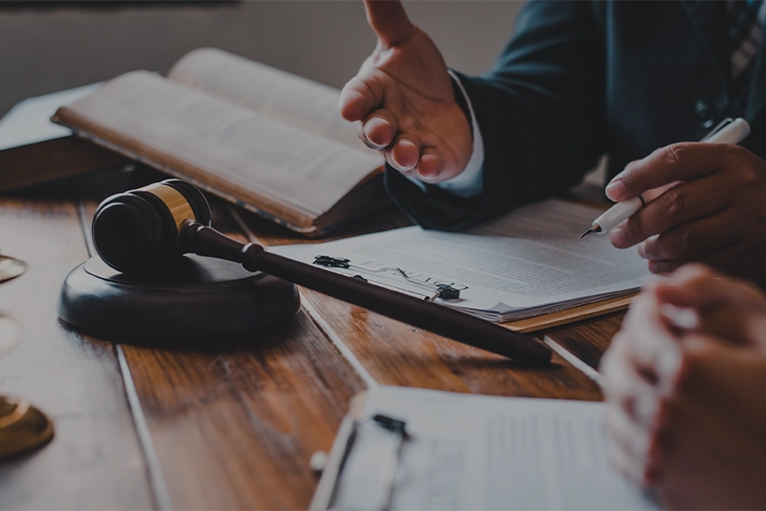 Close-up of a lawyer consulting a client with legal documents, gavel, and open law books on a wooden desk in an office.
