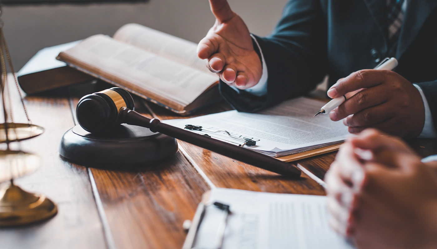 Close-up of a lawyer consulting a client with legal documents, gavel, and open law books on a wooden desk in an office.
