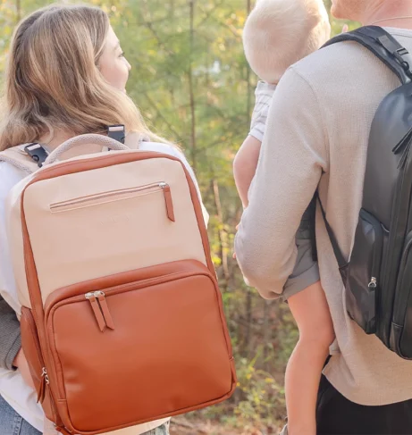 Parents carrying MAPAII diaper backpacks in neutral and black colors while holding their babies outdoors, showcasing stylish, functional, and gender-neutral designs for modern parenting on the go.