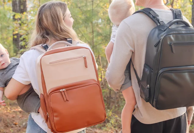Parents carrying MAPAII diaper backpacks in neutral and black colors while holding their babies outdoors, showcasing stylish, functional, and gender-neutral designs for modern parenting on the go.