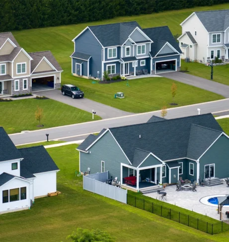 Suburban neighborhood with newly built modern homes, green lawns, and fenced backyards with pools.