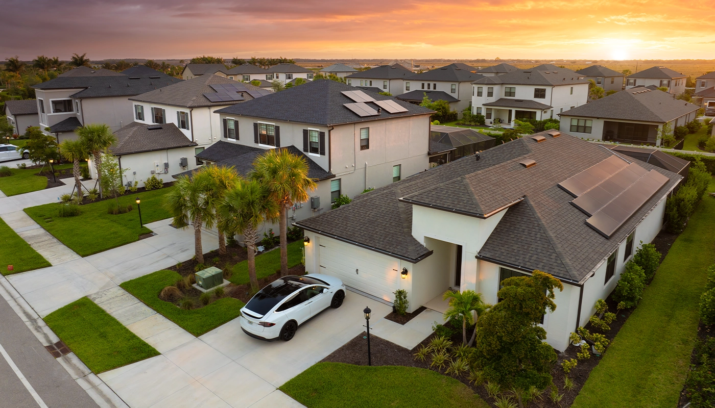 Modern suburban neighborhood with solar-powered homes and electric vehicles at sunset.