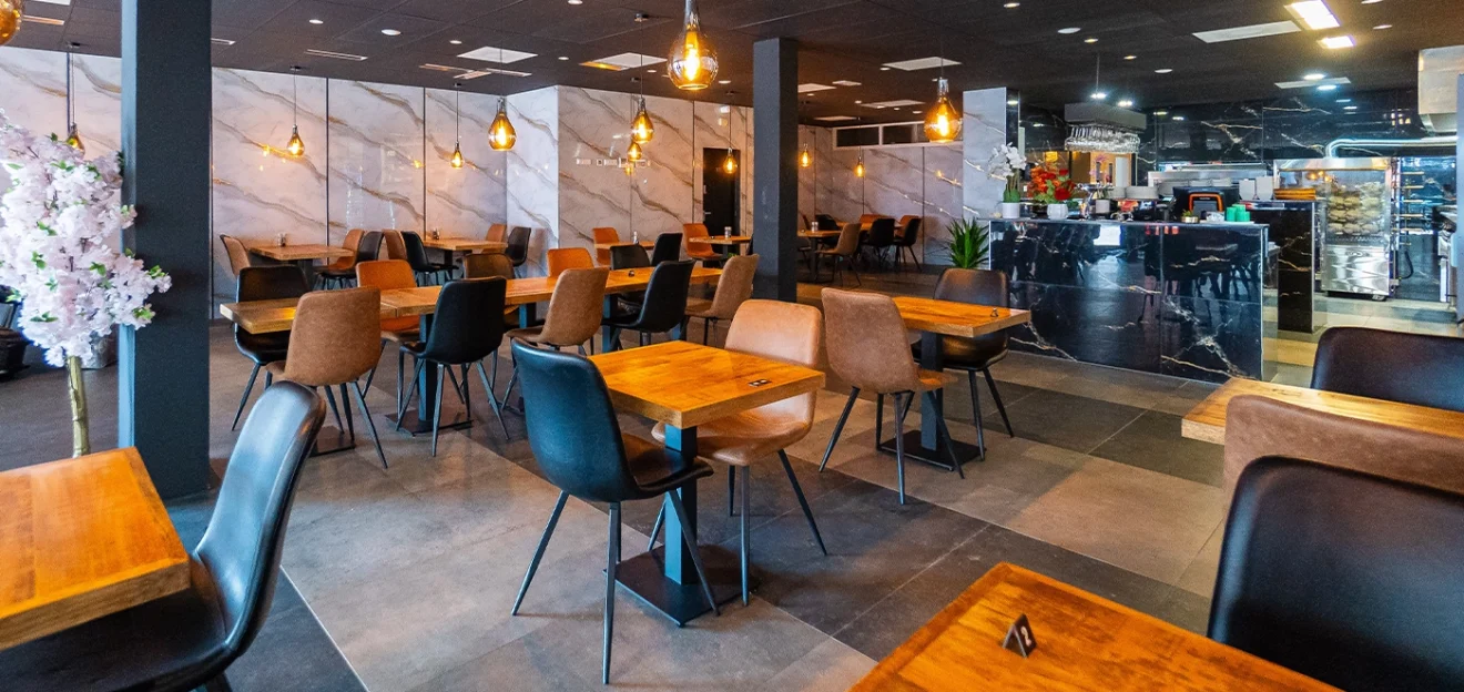 Modern restaurant interior with wooden tables, stylish chairs, and warm pendant lighting, featuring a marble counter and contemporary decor.