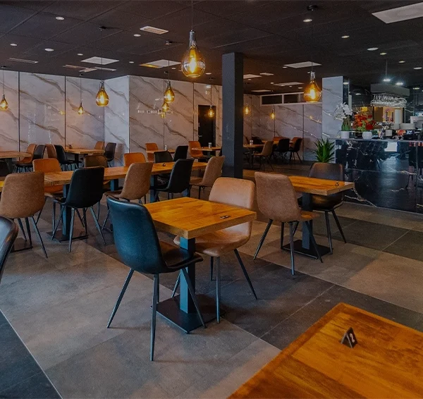 Modern restaurant interior with wooden tables, stylish chairs, and warm pendant lighting, featuring a marble counter and contemporary decor.