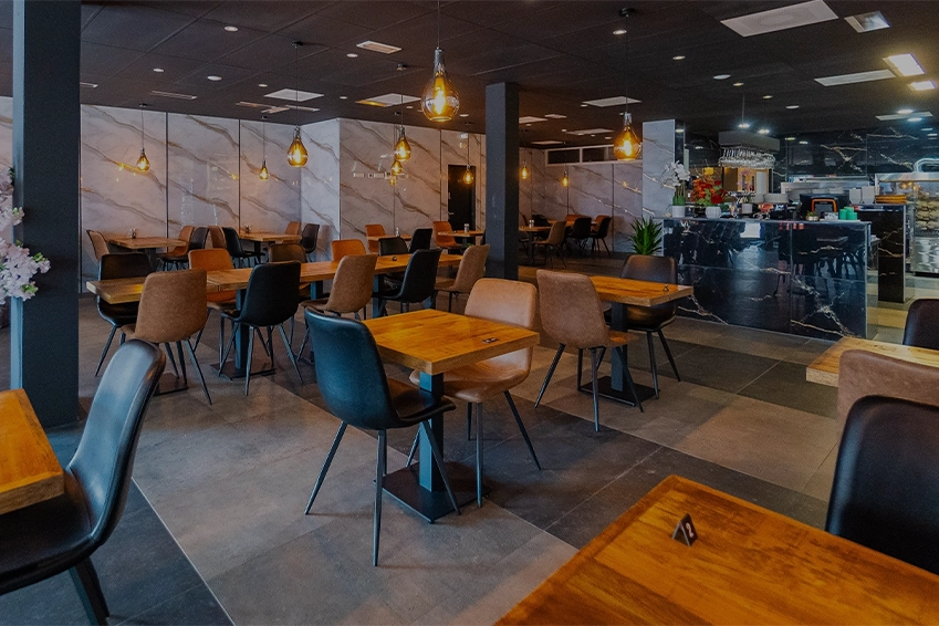 Modern restaurant interior with wooden tables, stylish chairs, and warm pendant lighting, featuring a marble counter and contemporary decor.