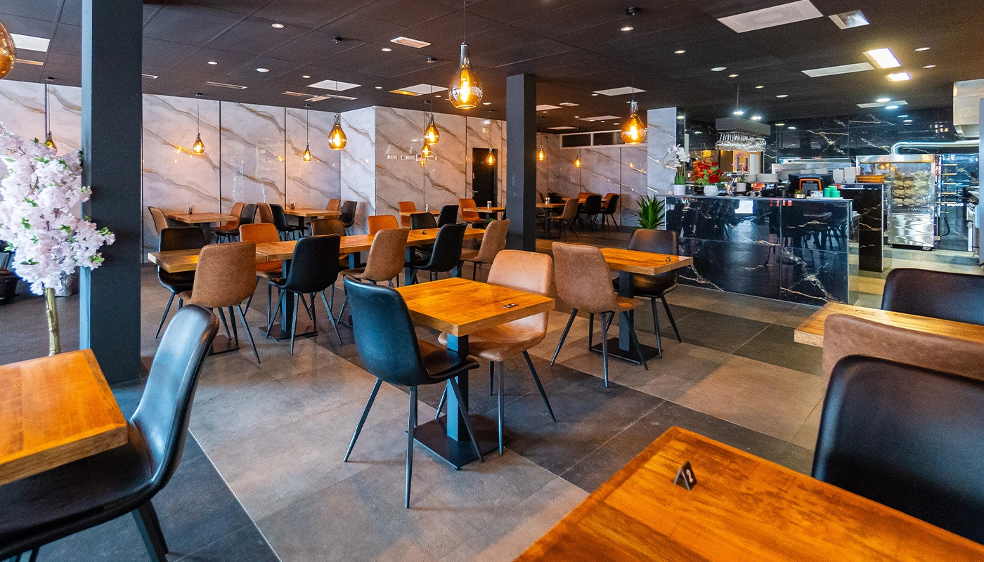 Modern restaurant interior with wooden tables, stylish chairs, and warm pendant lighting, featuring a marble counter and contemporary decor.