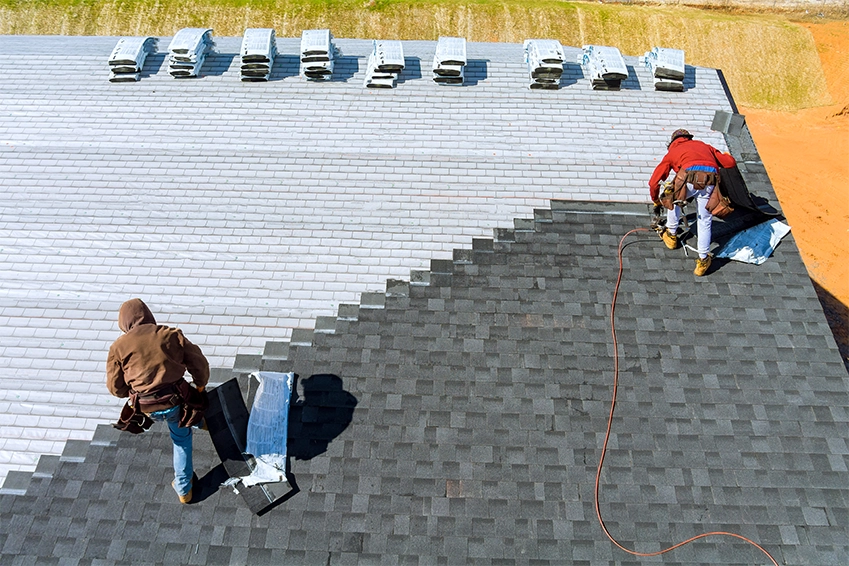 Roofing contractors installing dark shingles on a residential roof — professional roofing services branding.