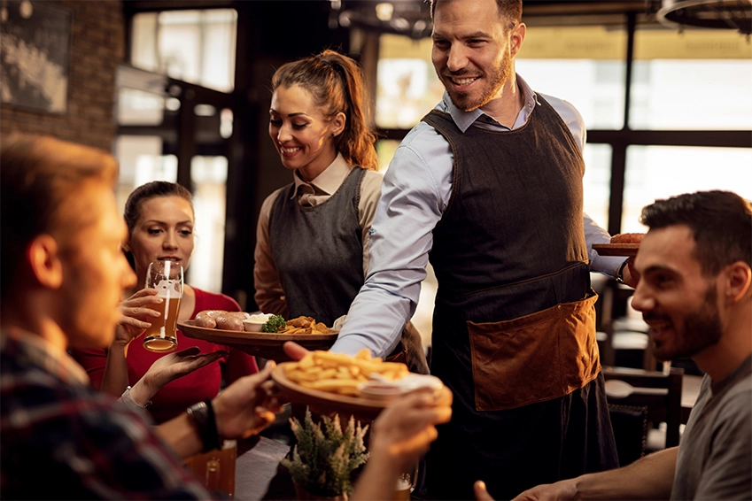 Restaurant servers delivering meals to smiling guests — hospitality branding and marketing photography.
